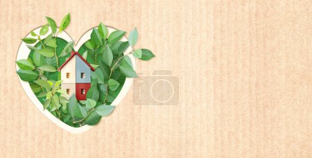 Eco friendly house. Wooden home model, heart shape hole and green leaves on cardboard texture. Ecology, go green, Green Energy, Renewable Power, environmental and conservation protection concept