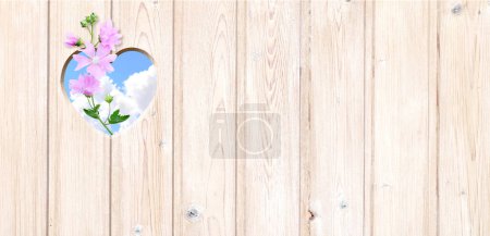 Photo for Heart-shaped hole in wooden boards, flower and blue sky with clouds. Heart shape hole in wood fence. Go green. Ecology, global ecological resource, eco and zero waste concept. Copy space for text - Royalty Free Image