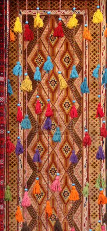 Foto de Cordones decorativos con borlas y alfombra tradicional iraní en el antiguo Gran Bazar, ubicado en el centro histórico del Isfahán, Irán. Cordones con borlas sobre fondo de alfombra oriental - Imagen libre de derechos