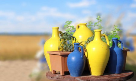 Photo for Rustic clay jugs of yellow and blue colors on wooden table on sunny nature background. Colourful traditional decorative jugs for wine on blurred backdrop of the countryside - Royalty Free Image