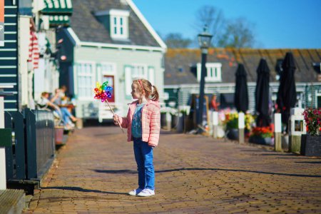 Photo for Adorable preschooler girl with colorful pinwheel walking in picturesque village of Marken near Volendam, North Holland, the Netherlands - Royalty Free Image