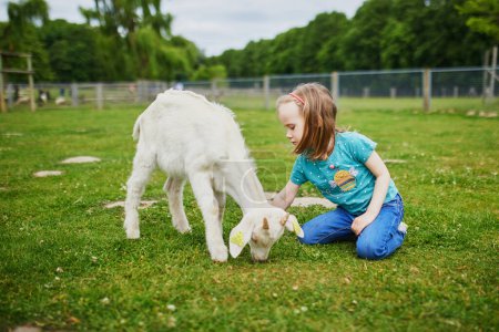 Foto de Adorable niña jugando con cabras y ovejas en la granja. Niña familiarizándose con los animales. Agricultura y jardinería para niños pequeños. Actividades al aire libre para niños - Imagen libre de derechos