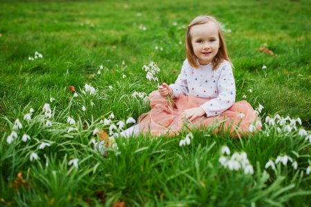 Photo for Cute preschooler girl in pink tutu skirt sitting in the grass with many snowdrop flowers in park or forest on a spring day. Little kid exploring nature. Outdoor activities for children - Royalty Free Image