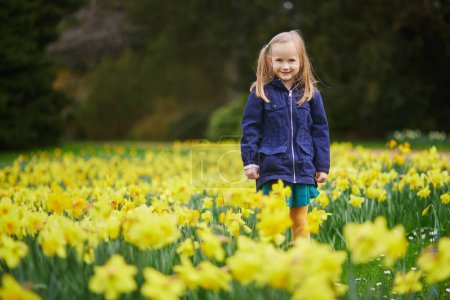 Foto de Adorable niña preescolar disfrutando de buen día de primavera en el parque durante la temporada de jonquils floreciente. Actividades de primavera al aire libre para niños. Niño pequeño explorando la naturaleza - Imagen libre de derechos