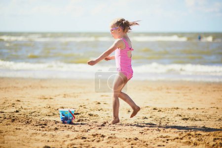 Téléchargez les photos : Petite fille d'âge préscolaire s'amusant sur la plage de sable sur la côte de la mer à Noordwijk, aux Pays-Bas. Activités d'été en plein air pour enfants - en image libre de droit