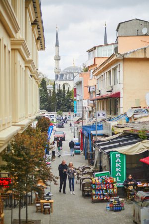 Foto de ISTANBUL, TURQUÍA - 23 DE ABRIL DE 2023: Gente caminando por una calle en el distrito de Uskudar con la mezquita Mihrimah Sultan al fondo en Estambul, Turquía - Imagen libre de derechos