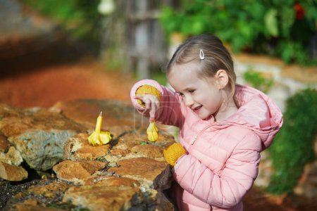 Téléchargez les photos : Fille d'âge préscolaire regardant comment les légumes poussent dans le jardin de cuisine. Enfant explorant la nature - en image libre de droit
