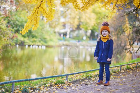 Téléchargez les photos : Adorable fille préscolaire profitant d'une belle journée d'automne ensoleillée en plein air. Joyeux enfant rassemblant des feuilles d'automne à Paris, France. Activités d'automne en plein air pour enfants - en image libre de droit