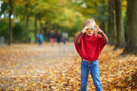 Téléchargez les photos : Adorable enfant d'âge préscolaire prenant une photo avec un appareil photo jouet en bois dans le parc d'automne à Paris, France. Joyeux enfant jouant avec des jouets dans le parc un jour d'automne. Enfant dégustant des collations saines à l'extérieur - en image libre de droit
