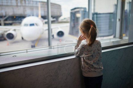 Téléchargez les photos : Enfant d'âge préscolaire à l'aéroport international, regardant par la fenêtre des avions. Concept Voyage avec enfants - en image libre de droit