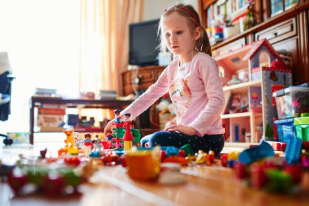 Photo for Adorable preschooler girl sitting on the floor and playing with colorful construction blocks. Indoor creative activities for kids - Royalty Free Image