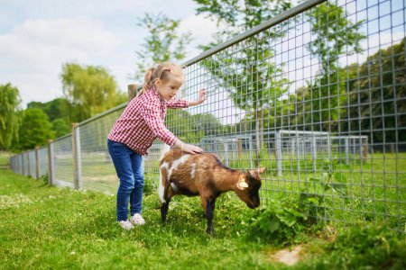 Photo for Adorable little girl playing with goats at farm. Child familiarizing herself with animals. Farming and gardening for small children. Outdoor summer activities for kids - Royalty Free Image