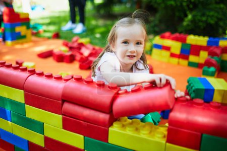 Photo for Adorable preschooler girl playing with large colorful plastic construction blocks outdoors, in kindergarten or preschool. Creative games for kids - Royalty Free Image