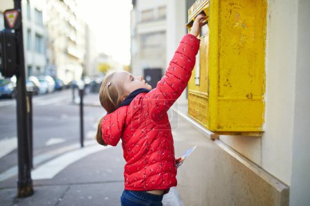 Photo for Adorable preschooler girl putting letter in yellow post box on a street of Paris, France - Royalty Free Image