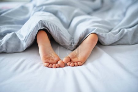 Photo for Little childs feet in bed covered with blanket. Kid sleeping in a comfortable bed. Early morning at home - Royalty Free Image