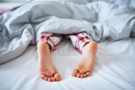 Téléchargez les photos : Petits enfants pieds dans le lit couvert de couverture. Il dort dans un lit confortable. Au petit matin à la maison - en image libre de droit
