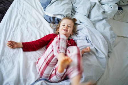 Photo for Happy preschooler girl wearing Christmas pajamas, playing on bed. Celebrating seasonal holidays with kids at home - Royalty Free Image