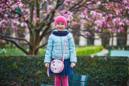 Photo for Adorable preschooler girl enjoying pink magnolias in full bloom on a rainy day in a park of Paris, France - Royalty Free Image