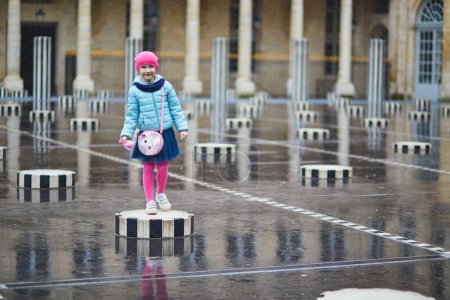 Photo for Adorable preschooler girl playing in Palais Royal garden on a rainy day. Child having fun in Paris, France. Happy kid playing outdoors - Royalty Free Image