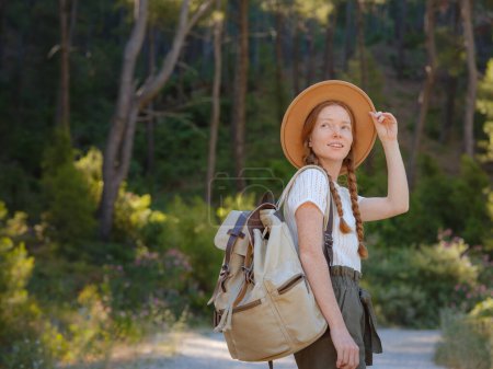 Photo for Caucasian ginger young beautiful female backpacker traveling alone in forest. Attractive traveler look around and explore while walk in nature wood with happiness and fun during holiday vacation trip. - Royalty Free Image