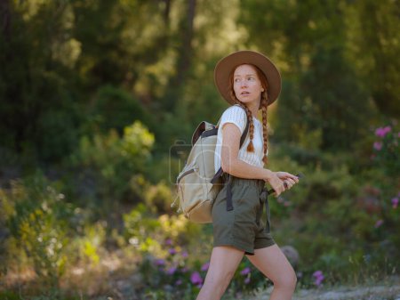 Téléchargez les photos : Gingembre caucasien jeune belle routeuse voyageant seule dans la forêt. Voyageur attrayant regarder autour et explorer tout en marchant dans le bois de la nature avec bonheur et plaisir pendant le voyage de vacances. - en image libre de droit