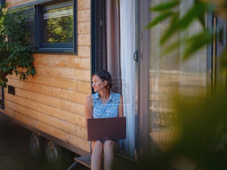 Photo for Happy young asian woman with laptop resting outdoors near tiny house, weekend away and remote office idea. Tiny houses and Small Living concept. summer garden - Royalty Free Image