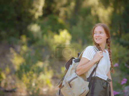 Téléchargez les photos : Gingembre caucasien jeune belle routeuse voyageant seule dans la forêt. Voyageur attrayant regarder autour et explorer tout en marchant dans le bois de la nature avec bonheur et plaisir pendant le voyage de vacances. - en image libre de droit