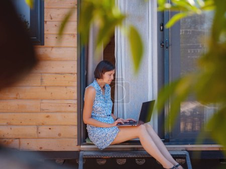 Photo for Happy young asian woman with laptop resting outdoors near tiny house, weekend away and remote office idea. Tiny houses and Small Living concept. summer garden - Royalty Free Image