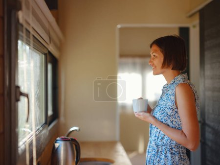 Photo for Young woman enjoying cup of coffee at morning, in her kitchen. Minimalism. Moving in. Living alone. Charming trailer house - Royalty Free Image