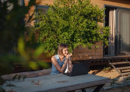 Photo for Happy young asian woman with laptop resting outdoors in tiny house in summer garden, weekend away and remote office idea, early morning. Tiny houses and Small Living concept. - Royalty Free Image