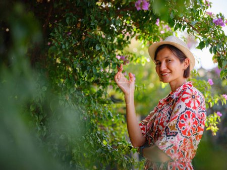 jeune femme asiatique se tient dans un parc verdoyant ensoleillé, admirant la floraison buisson de bougainvilliers. Les fleurs couleurs vives sont beaux contraste avec les parcs verdure luxuriante.
