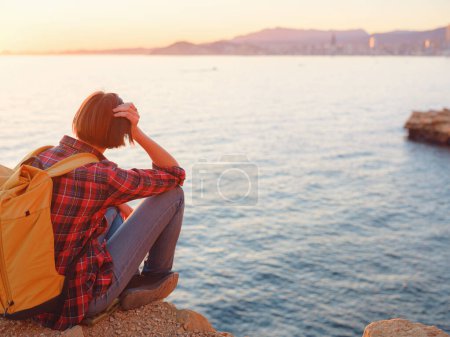 Junge Frau beim Wandern am felsigen Strand von Benidorm in Spanien. Beobachtet das abgehackte Meer und die Bucht. Reisende genießen Freiheit in ruhiger Naturlandschaft