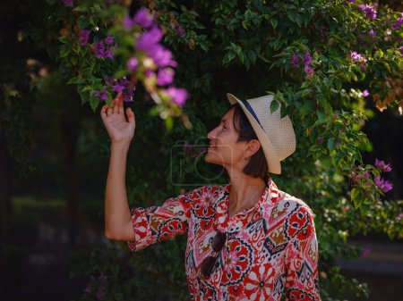 jeune femme asiatique se tient dans un parc verdoyant ensoleillé, admirant la floraison buisson de bougainvilliers. Les fleurs couleurs vives sont beaux contraste avec les parcs verdure luxuriante.