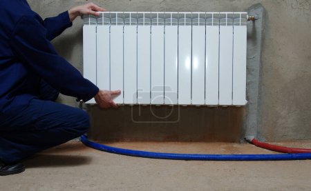 Téléchargez les photos : Un plombier en combinaison bleue répare un radiateur - en image libre de droit