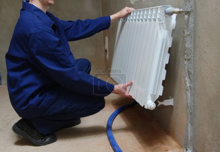 Téléchargez les photos : Un plombier en combinaison bleue répare un radiateur - en image libre de droit