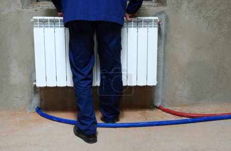 Foto de Un fontanero con un mono azul está arreglando un radiador - Imagen libre de derechos