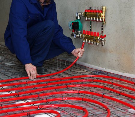 Foto de Trabajador está instalando una tubería roja para el suelo caliente montaje del sistema de calefacción por suelo radiante - Imagen libre de derechos