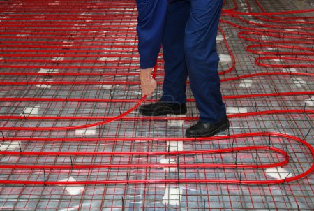 Photo for Worker is installing a red pipe for the warm floor mounting the system underfloor heating - Royalty Free Image