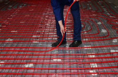 Téléchargez les photos : Travailleur installe un tuyau rouge pour le montage au sol chaud du système de chauffage par le sol - en image libre de droit