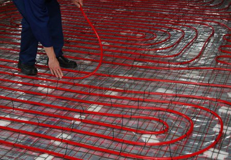 Foto de Trabajador está instalando una tubería roja para el suelo caliente montaje del sistema de calefacción por suelo radiante - Imagen libre de derechos