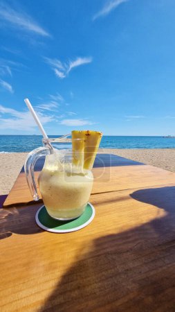 A drink resting on a wooden table placed next to the ocean, with waves crashing in the background.