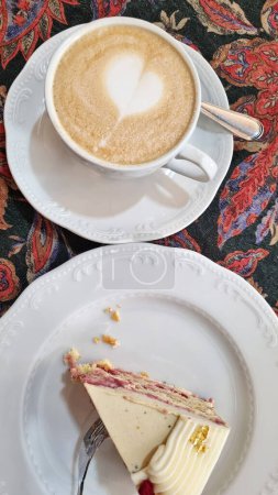 A piece of cake resting on a plate next to a cup of coffee on a table.