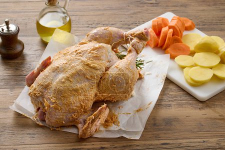 Foto de Pollo crudo cubierto con mantequilla picante y verduras en la mesa de la cocina de madera. proceso de elaboración de pollo asado - Imagen libre de derechos