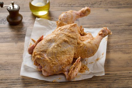 Foto de Pollo crudo cubierto con mantequilla picante en la mesa de la cocina de madera. proceso de elaboración de pollo asado - Imagen libre de derechos