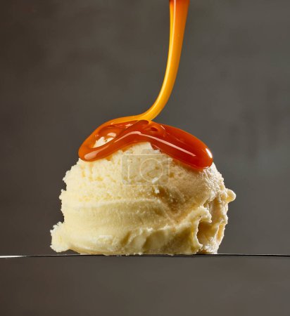 Foto de Vanilla ice cream ball with caramel sauce on grey background - Imagen libre de derechos