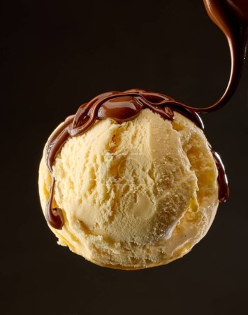 Photo for Vanilla ice cream ball with pouring melted chocolate sauce on black background - Royalty Free Image