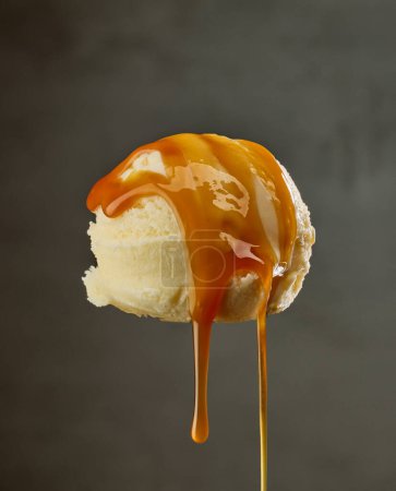 Photo for Vanilla ice cream ball with pouring caramel sauce on dark grey background - Royalty Free Image