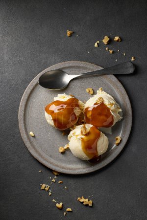 Téléchargez les photos : Plate of vanilla ice cream with caramel sauce and walnut on dark grey background, top view - en image libre de droit