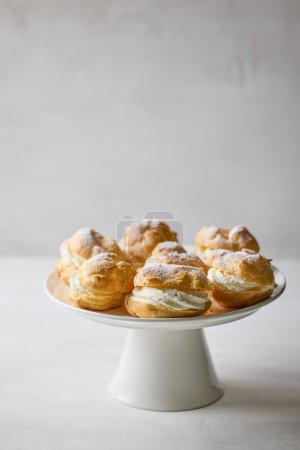 Photo for Plate of cream puffs decorated with powdered sugar on light grey background - Royalty Free Image