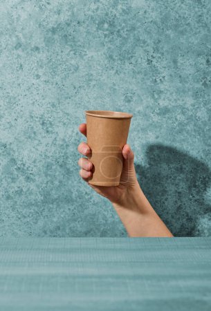 Téléchargez les photos : Paper take away coffee cup in human hand on blue background - en image libre de droit